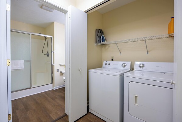 Une buanderie équipée d’une cabine de douche en verre, d’un lave-linge blanc et d’un sèche-linge.