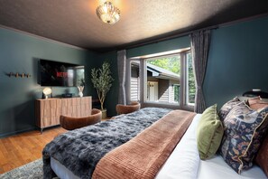 A bedroom with a bed, a television, a plant, and a window.