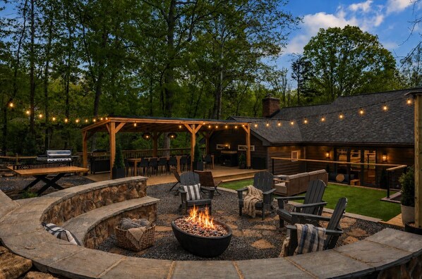 A covered outdoor seating area with a fire pit, stone seating, and string lights.