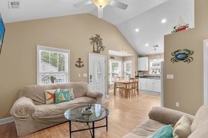 A living room with a beige sofa, a glass coffee table, and a dining area with wooden chairs. - Spacious Home in Ocean Lakes. Outdoor entertainment, and Gated covered deck. (Myrtle Beach)