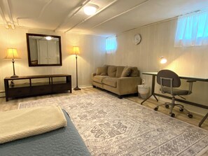 A room with a bed, a sofa, a desk with a chair, a lamp, a mirror, and a clock on the wall. - TUFTS - Quiet Furnished Apt w/All Included (Medford)