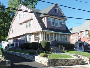 A two-story house with a stone foundation, a front porch, and a staircase leading to the entrance. - TUFTS - Quiet Furnished Apt w/All Included (Medford)