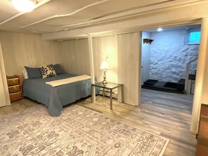 A bedroom with a bed, bedside table, lamp, and a patterned rug. - TUFTS - Quiet Furnished Apt w/All Included (Medford)
