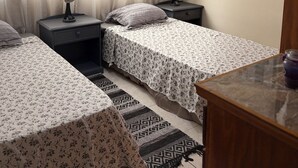 Une chambre avec deux lits, une table de chevet avec une lampe, une fenêtre avec des rideaux et un tableau au mur.