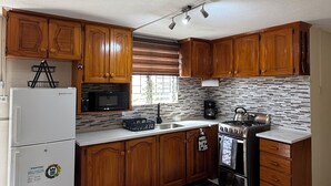 Une cuisine avec des meubles en bois, un réfrigérateur blanc, un four à micro-ondes, une cuisinière et une fenêtre avec des stores.