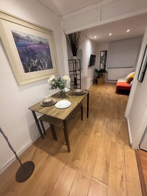 A dining area with a wooden table, white plates, and a vase of flowers. There is a framed painting on the wall and a plant in a black pot. - Entire Cosy Home in the meadows, free parking, close to city centre (Nottingham)