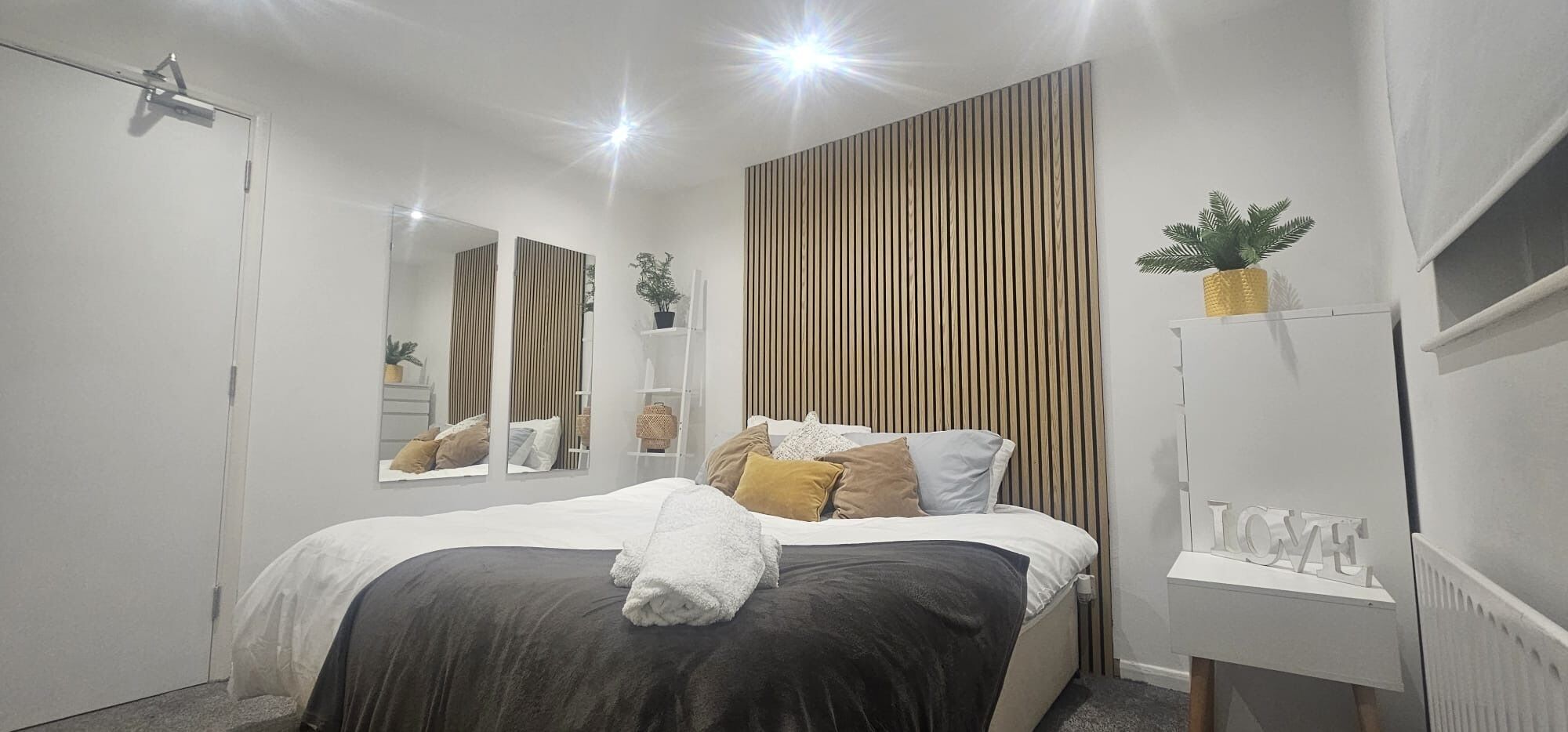A modern bedroom with a bed, bedside tables, a mirror, and a wall-mounted radiator.