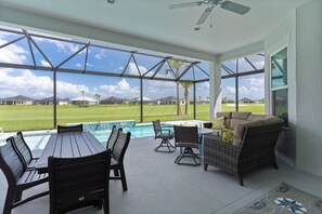 A covered outdoor area with a pool, seating, and a view of a golf course. - Edenfield Golfview Retreat (Sumterville)