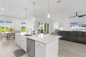 A modern kitchen with a central island, a dining area with a table and chairs, and a living room with a sofa and a television. - Edenfield Golfview Retreat (Sumterville)