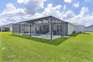 Una casa con porche cubierto, piscina y jardín.