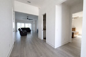 A spacious living area with a dark-colored sofa, a ceiling fan, and a kitchen area visible through an open door. - Edenfield Golfview Retreat (Sumterville)