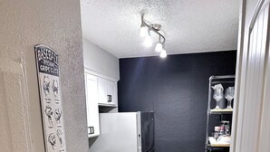 Una cocina compacta con refrigerador, lavavajillas y una lámpara fijada a la pared.