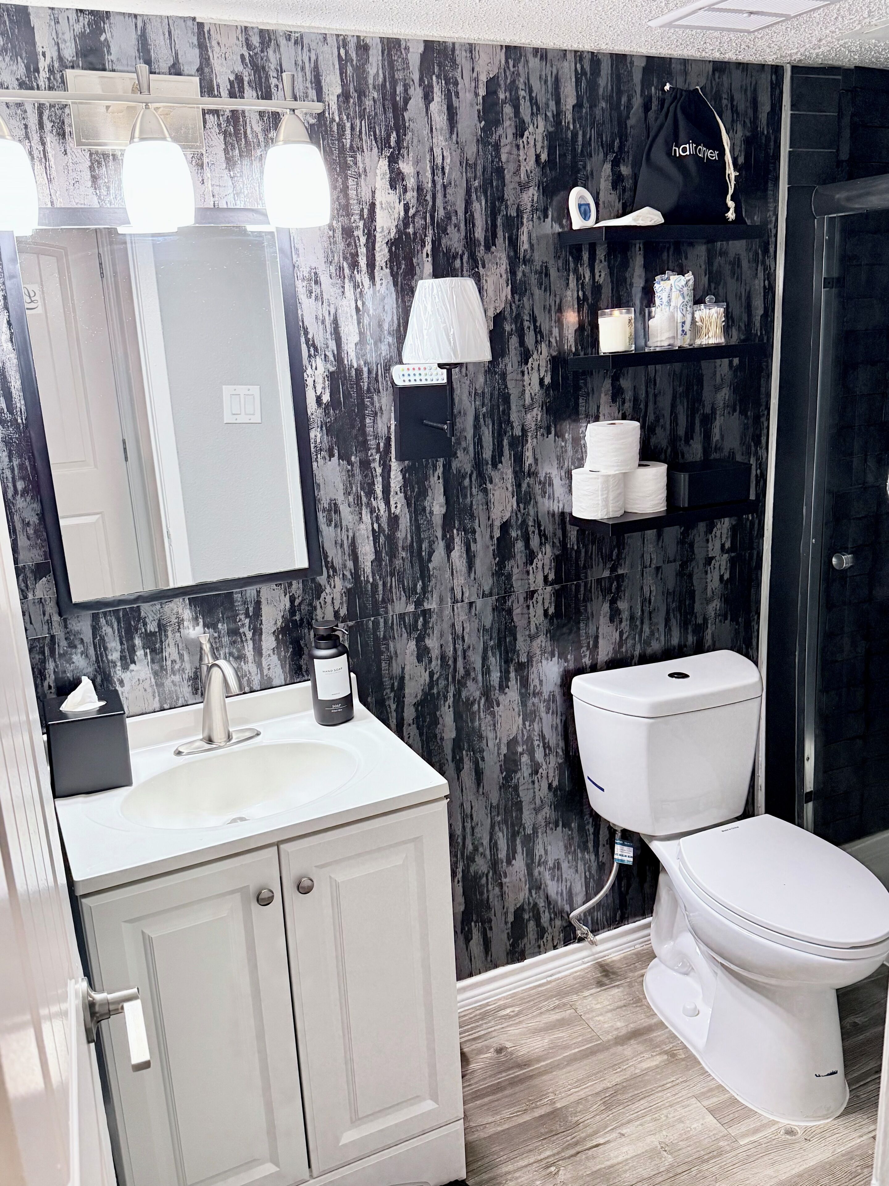 Un baño moderno con un lavabo blanco, un espejo, un inodoro y un estante con artículos de aseo.