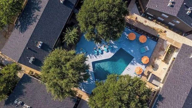 Vista aérea de una zona residencial con piscina, rodeada de árboles y algunos coches estacionados.