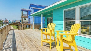 Una terraza de madera con sillas Adirondack amarillas, un edificio azul con detalles blancos y una valla de madera.