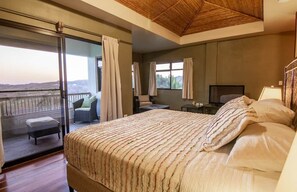 A bedroom with a large bed, a TV, a desk, and a balcony with a view.
