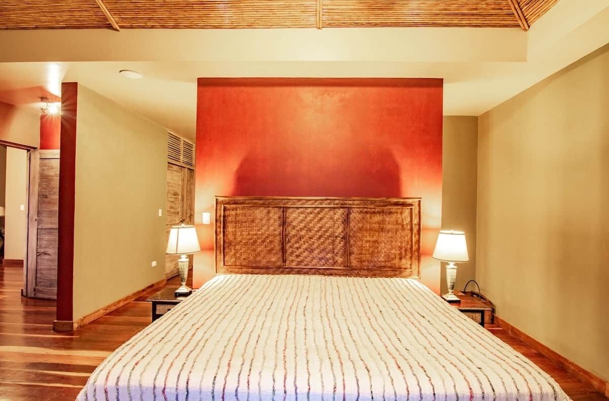 A hotel room with a large bed, wooden headboard, two bedside lamps, and a red accent wall.