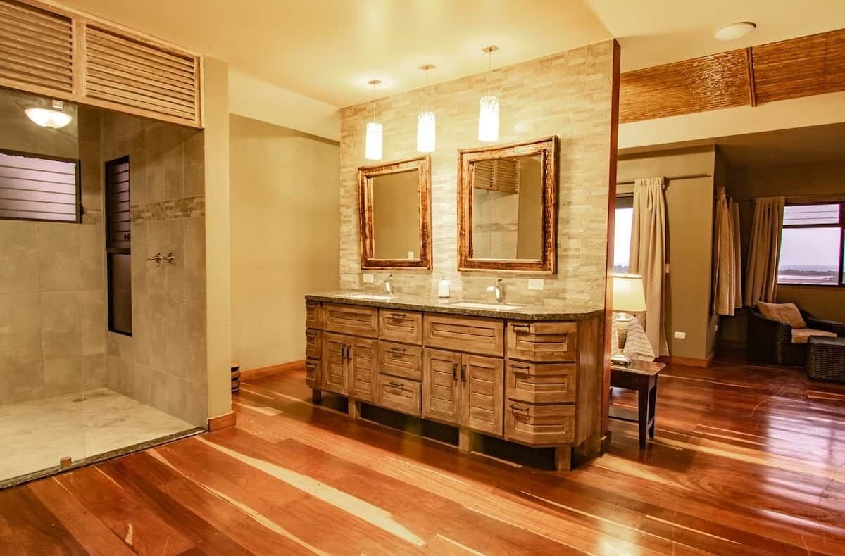 A bathroom with a shower, wooden vanity, two mirrors, and a window.