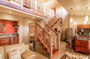 A spacious living area with a high ceiling, a staircase, a kitchen with modern appliances, and a balcony.