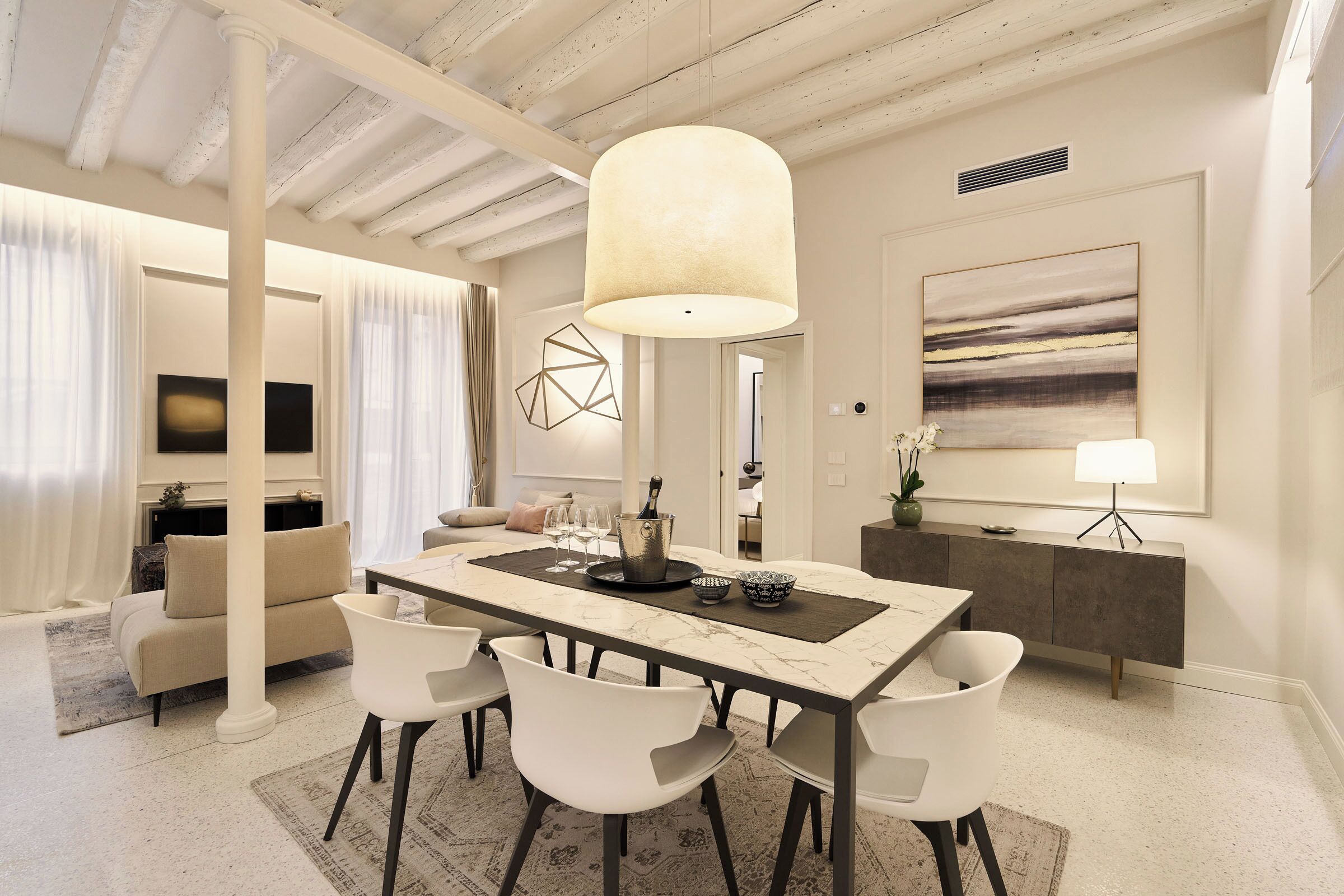 A modern dining area with a marble table, white chairs, a pendant light, and a minimalist decor.