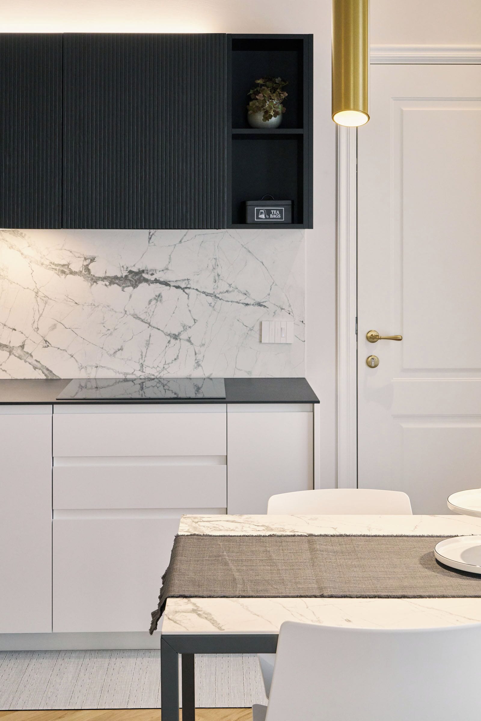 A modern kitchen with a marble backsplash, a dark upper cabinet, and a gold pendant light.