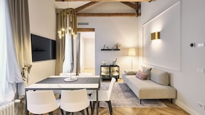 Una sala de estar moderna con una mesa de comedor, sillas blancas, un sofá y un televisor en la pared.