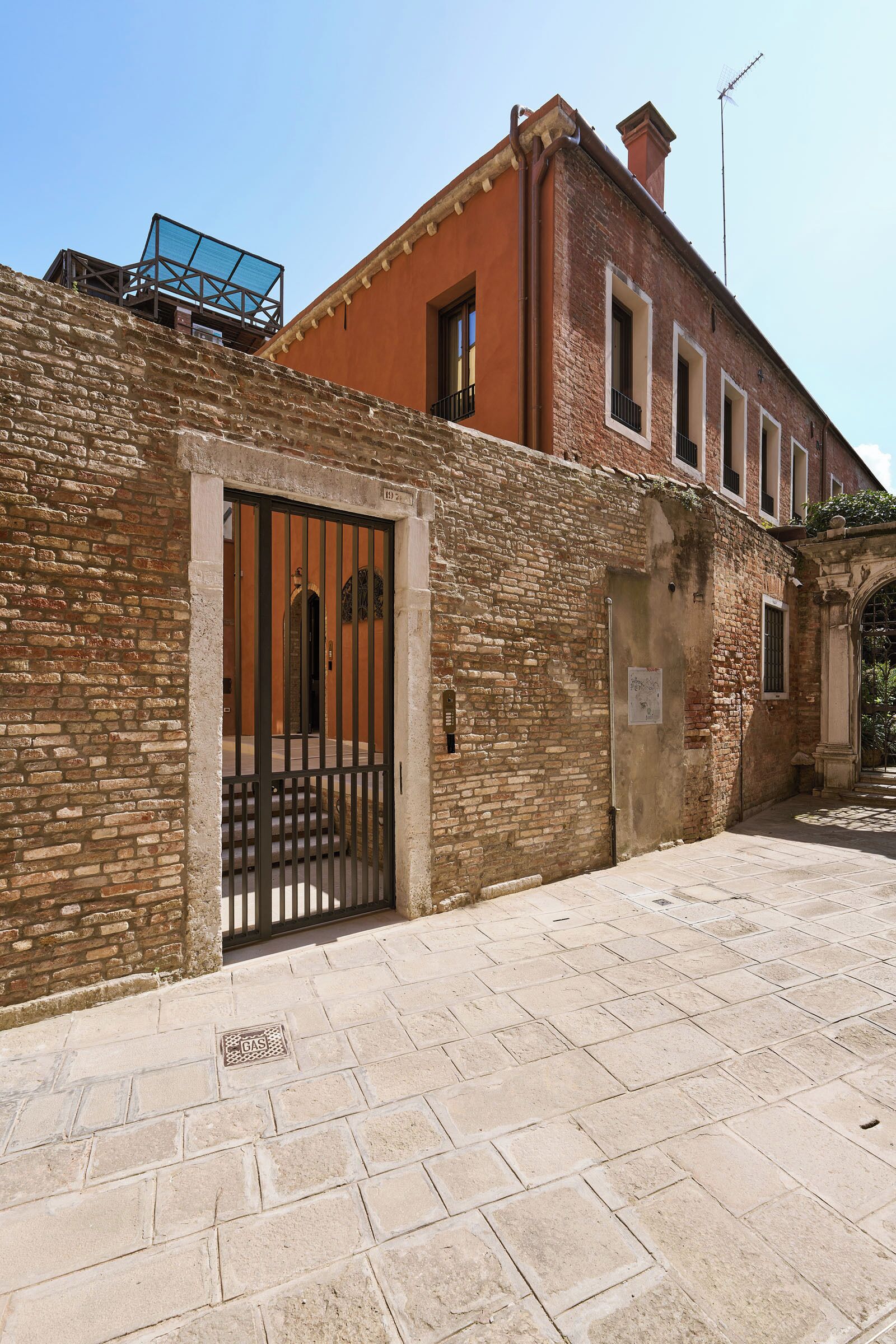 A stone building with a metal gate, a brick wall, and a clear sky.