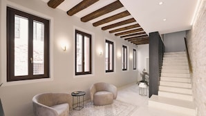 Un vestíbulo amplio con ventanas grandes, una escalera y dos sillones.