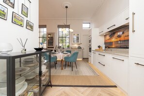 Une cuisine moderne avec des meubles blancs, un coin repas doté d’une table ronde et de chaises, et une grande fenêtre offrant une vue sur l’extérieur.