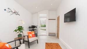 A modern living room with a flat-screen TV, a sofa, a chair, a small table, a lamp, and a plant. - One Bedroom Retreat in Prime Location - Pass the Keys (Bath)