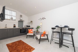 A modern kitchen with grey cabinets, a built-in oven, and a large window. There are two chairs and a table with stools, a rug, and a wall-mounted light fixture. - One Bedroom Retreat in Prime Location - Pass the Keys (Bath)
