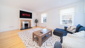 Een woonkamer met een open haard, een bank, een bijzettafeltje en een groot raam.