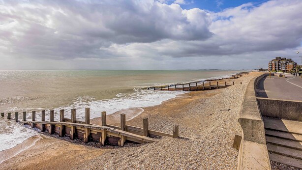 A beach with a wooden jetty, a concrete walkway, and a building in the background.
