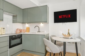 A modern kitchen with a built-in oven, a sink, and a dining area with a table and chairs. A television mounted on the wall displays the word 'NETFLIX.' - Dreamy Leeds Centre Retreat – Ideal for Couples - Pass the Keys (Leeds)