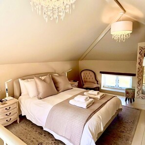 Ein Schlafzimmer mit Bett, Nachttischen, einem Sessel, einem Fenster und einer Chandelier.
