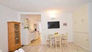 Een compacte leefruimte met een kitchenette, een eethoek en een aan de muur bevestigde televisie.