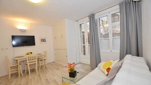 Een woonkamer met een bank, een televisie, een eettafel met stoelen en een raam met gordijnen.
