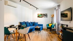 Un soggiorno moderno con un divano blu, un tavolo da pranzo con sedie, una TV e opere d'arte alle pareti.