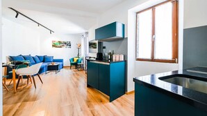 Una cucina moderna con isola centrale, zona pranzo con divano blu e un'ampia finestra che lascia entrare luce naturale.