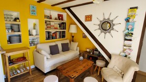 Ein gemütliches Wohnzimmer mit Sofa, Sessel, Couchtisch aus Holz und einer Bücherwand mit Büchern und Dekoration.