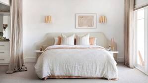 Een slaapkamer met een groot bed, nachtkastjes, een spiegel en gordijnen.