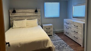 Une chambre à coucher comprenant un lit, des tables de chevet, une commode et une fenêtre avec des stores.