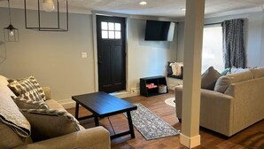 Un salon avec un canapé, une table basse, un téléviseur fixé au mur et une porte.