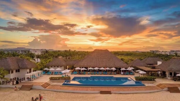 Un resort con piscina, construcciones de techo de paja y vistas al atardecer.