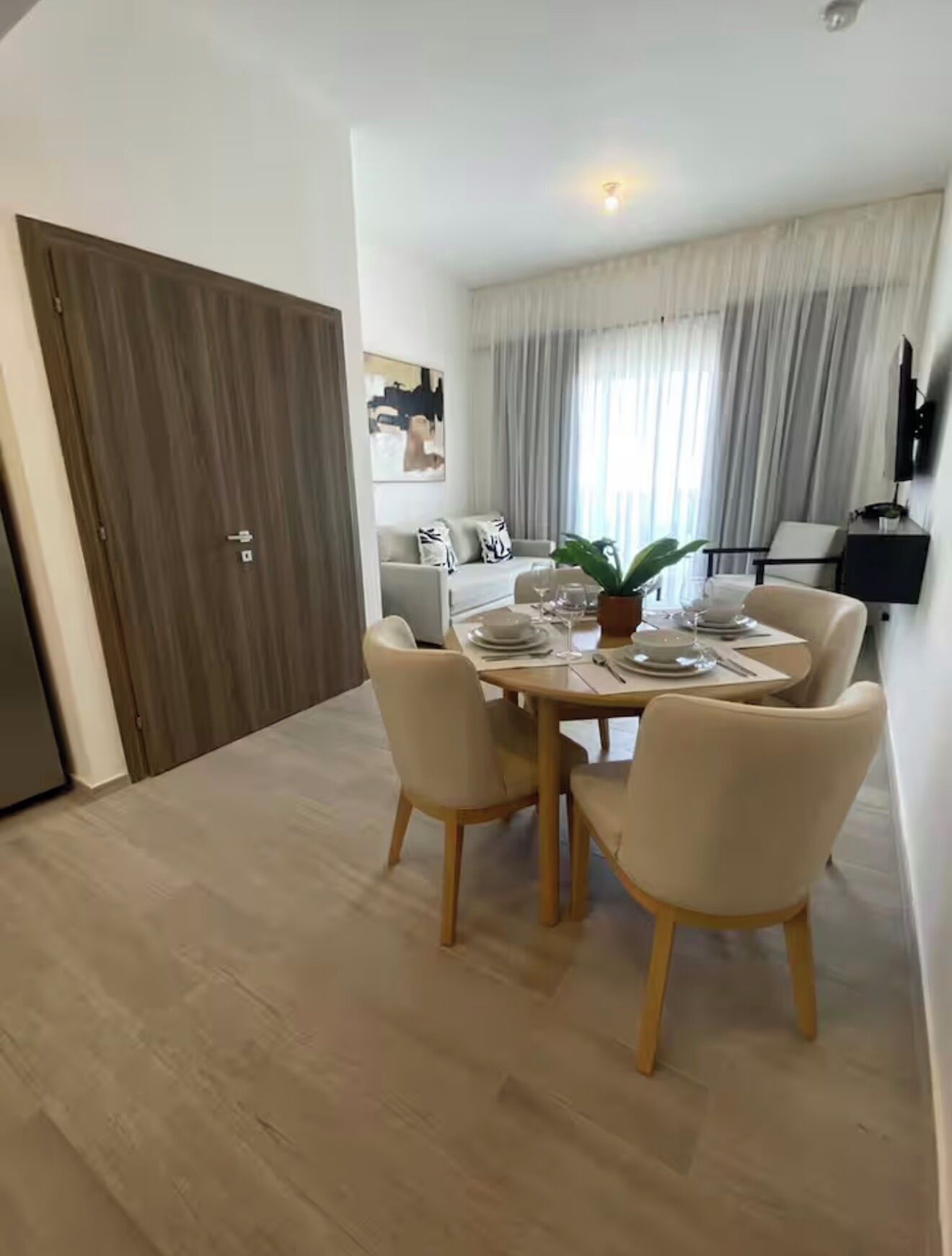 Un coin repas avec une table dressée pour quatre personnes, un canapé, un téléviseur et une porte.