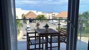 Un balcón con mesa y sillas, una planta en maceta y vista a un estacionamiento y edificios.