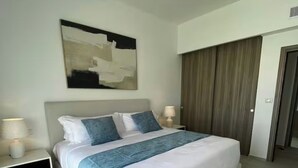 Una habitación de hotel moderna con una cama grande, una mesita de noche, un cuadro abstracto en la pared y una puerta de madera.