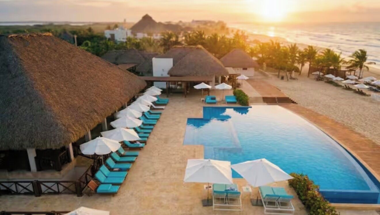 Un complexe hôtelier doté d’une piscine, de chaises longues et de cabanes à toit de chaume.