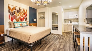 A modern bedroom with a bed, a chandelier, and a view into the kitchen. - Desert Studio Fast WiFi Gym & Kitchen (Tolleson)