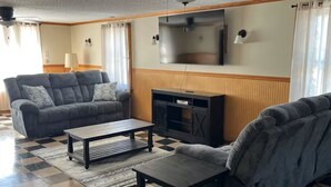 A living room with a sofa, a coffee table, a flat-screen TV, and a fireplace. - Narrowsburg Inn Vacations (Narrowsburg)